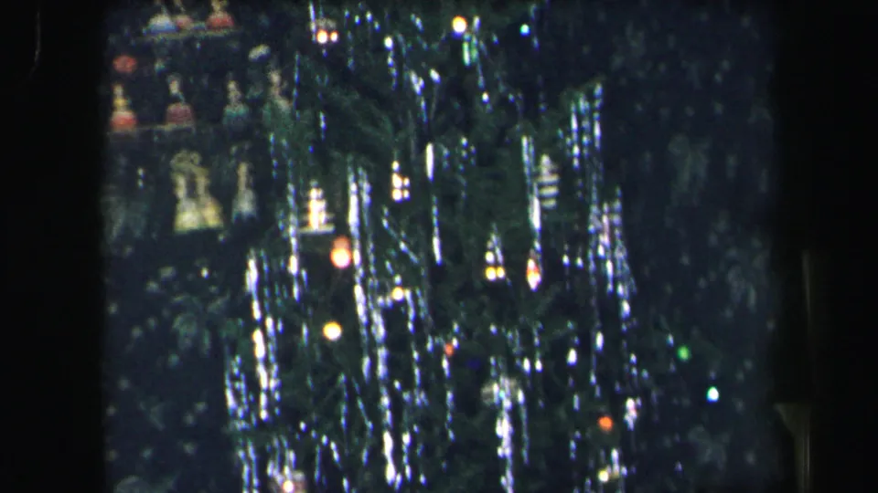 1975 Lynbrook holiday frame emphasizing dense tinsel, dim tree branches, and scattered colored Christmas lights.