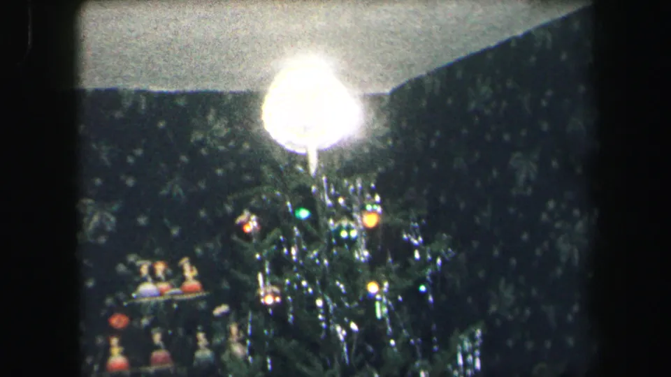 1975 Lynbrook 8mm frame showing a lit Christmas tree, reflective tinsel, a bright lamp, and small decorations nearby.