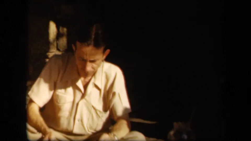 In 1943 Skyline Drive home-movie footage, a seated man in a light short-sleeved shirt looks down in dim outdoor light.