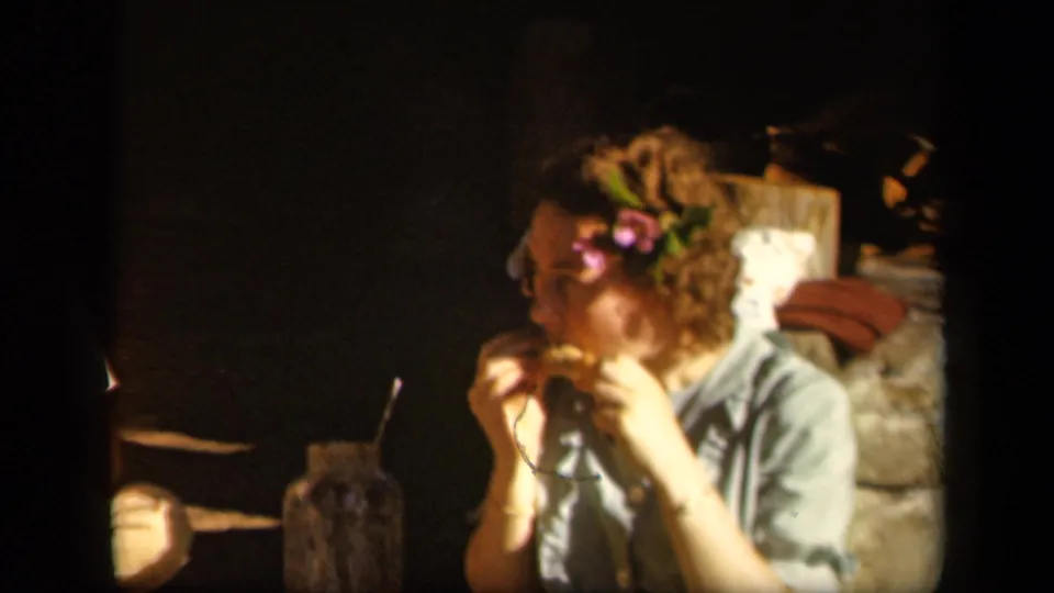 In 1943 home-movie footage, a young woman with flowers in her hair appears to eat a snack in a shaded setting at Skyline Drive, Virginia.