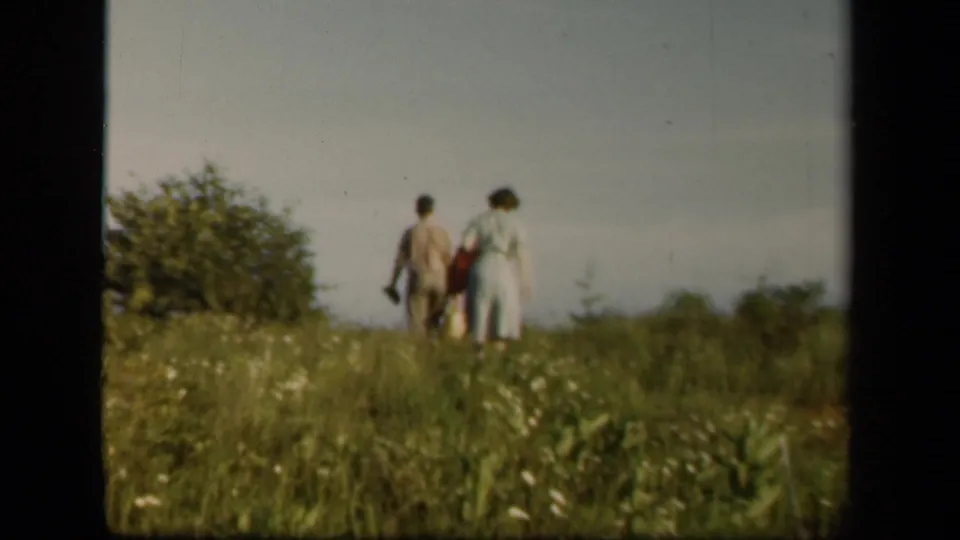 Two adults on Skyline Drive, Virginia, walk through a tall meadow with bags in 1943 home-movie footage.