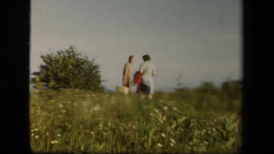 The couple continues across the Skyline Drive meadow, with bags visible against tall grass and low shrubs.