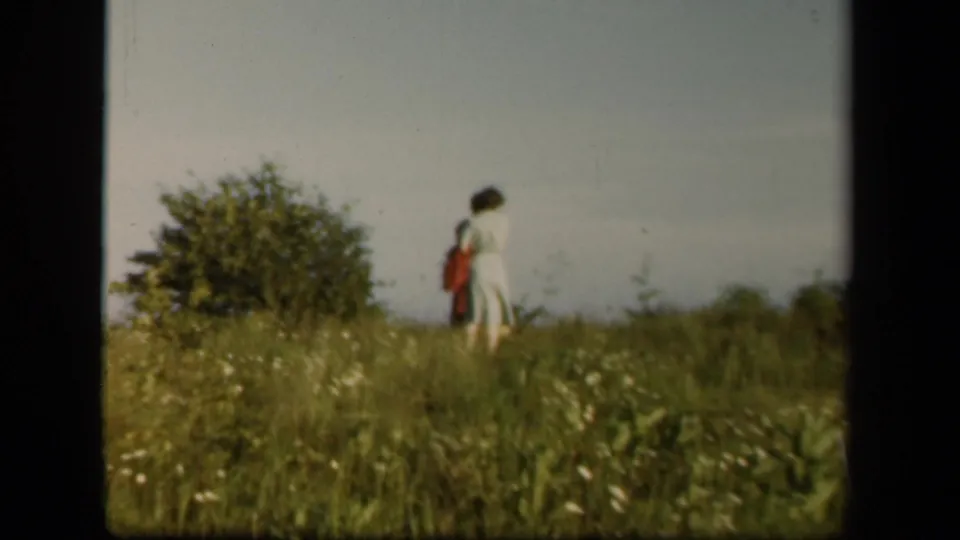 A woman in a light dress is seen in the meadow, carrying or standing near a red-toned bag in 1943 Virginia footage.