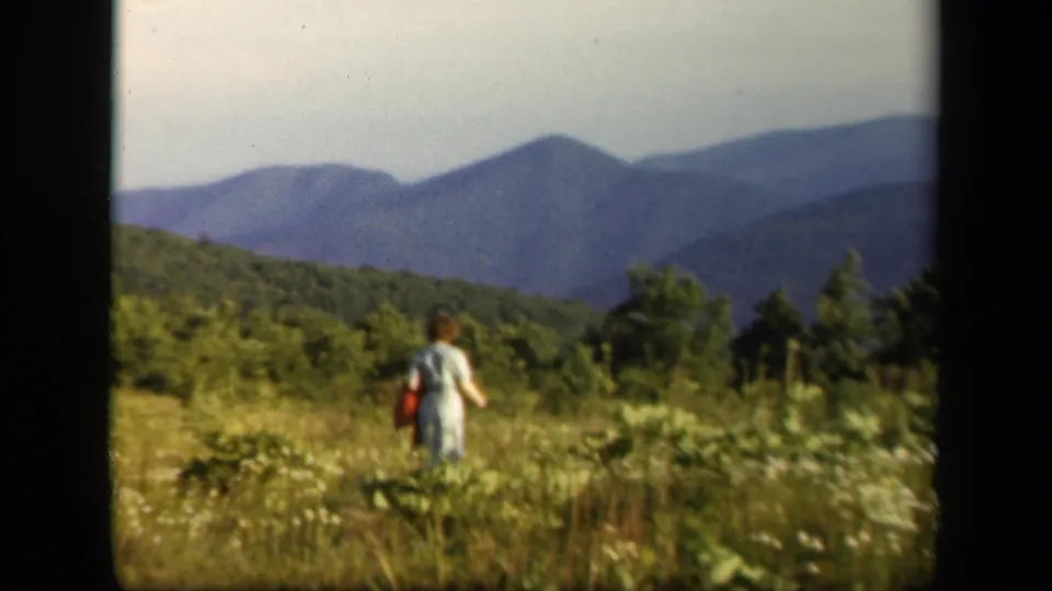 Late clip frame from the 1943 Skyline Drive home movie, showing the woman farther into the meadow with wooded Blue Ridge scenery behind.