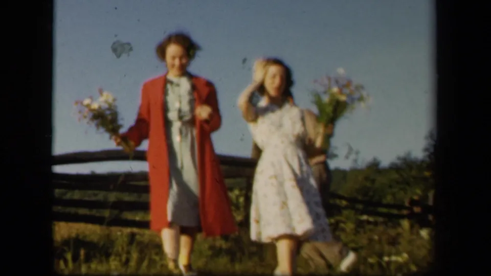 Two women walk toward the camera with bouquets along Skyline Drive, Virginia, in metadata-supported 1943 home-movie footage.