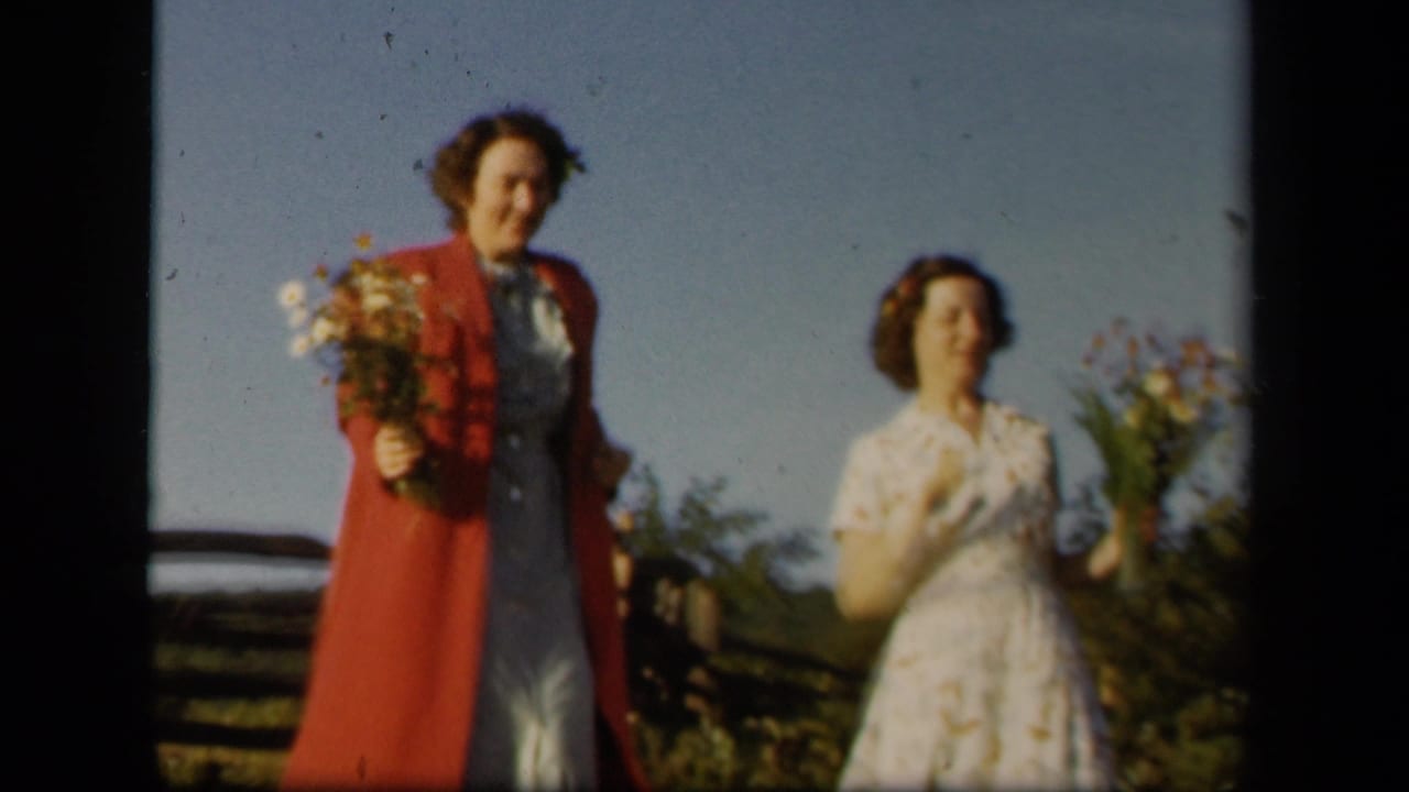 Two women continue toward the camera with wildflower bouquets near a fence in 1943 Skyline Drive home-movie footage.