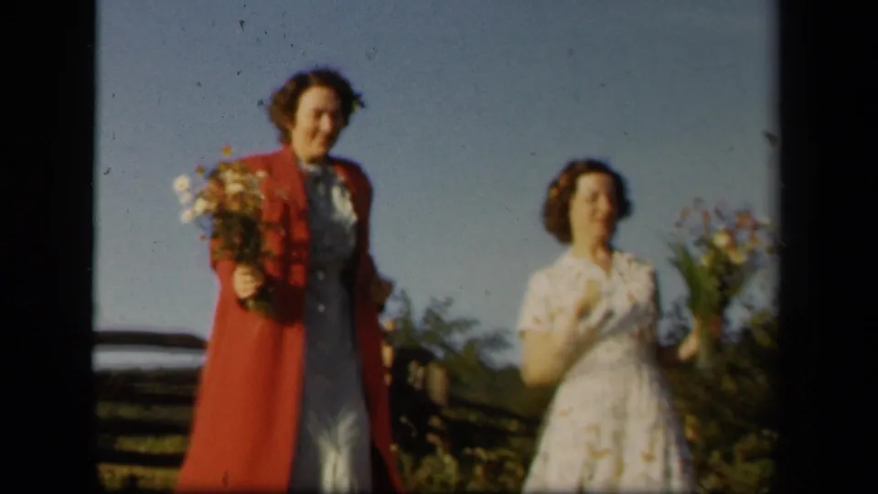Two women continue toward the camera with wildflower bouquets near a fence in 1943 Skyline Drive home-movie footage.