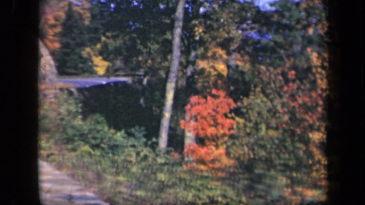 1943 Skyline Drive footage shows a curved mountain road bordered by stonework, rocky slope, and red-orange fall foliage.