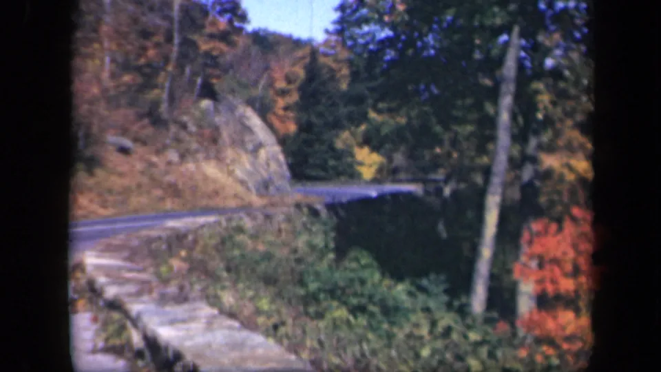 The 1943 home-movie view shows Skyline Drive curving past a rocky embankment with autumn trees and dense roadside greenery.