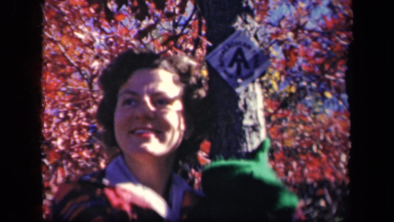Woman smiling near a tree and trail marker in autumn woods.