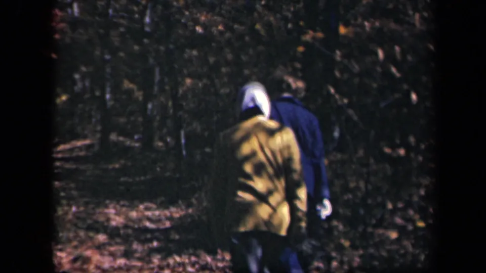 Two women, one in a yellow jacket and one in blue, walk away on a shaded wooded path at Skyline Drive, Virginia.