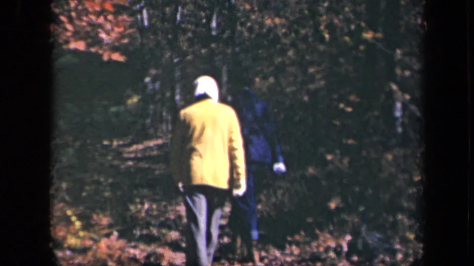 1943 Skyline Drive home-movie frame showing hikers from behind on a forest path, one wearing a yellow jacket and white head covering.
