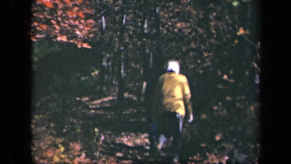 1943 Skyline Drive home-movie frame showing a rear-view hiker on a leaf-strewn path in dense forest light.