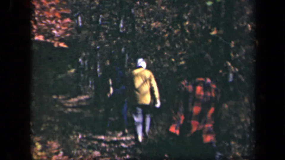 1943 Skyline Drive home-movie frame showing three hikers from behind on a leaf-strewn forest path in autumn light.