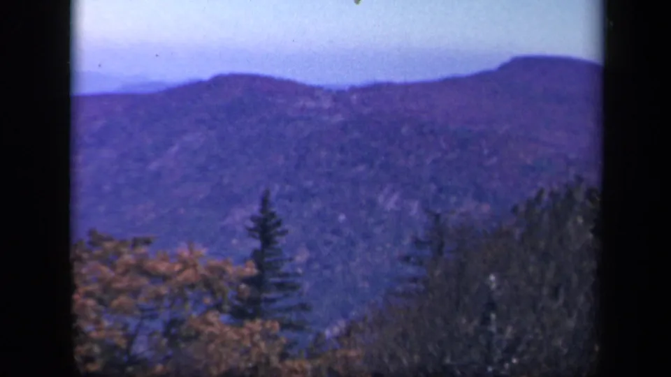 1943 Skyline Drive home-movie frame showing a blue mountain ridge beyond foreground evergreens and fall foliage.