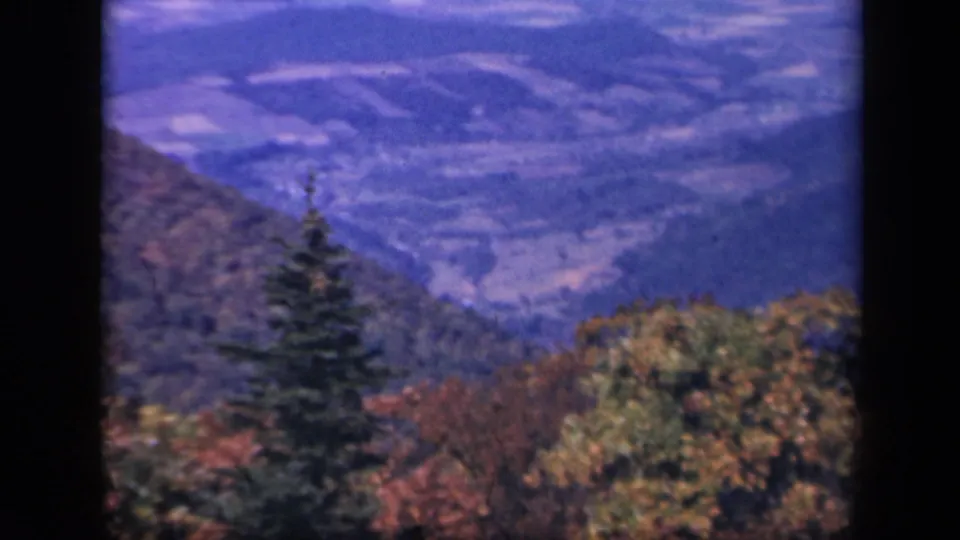 1940s home-movie view from Skyline Drive showing a valley, layered ridges, and foreground fall foliage.