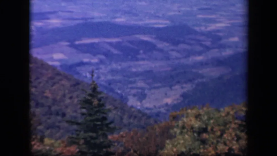Skyline Drive scenic overlook frame with distant ridges, valley patterns, and fall foliage in soft 8mm color.