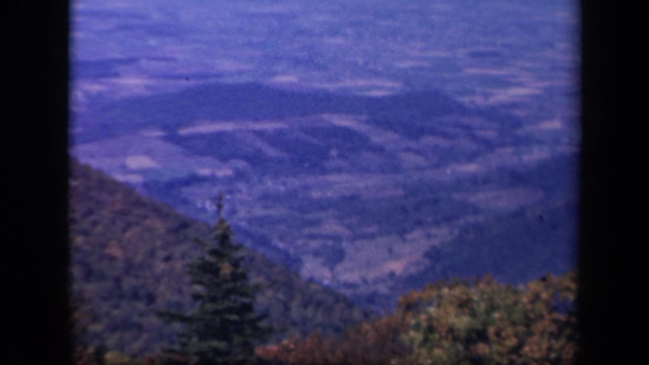 Forested mountain slopes and distant valley fields under a blue sky.