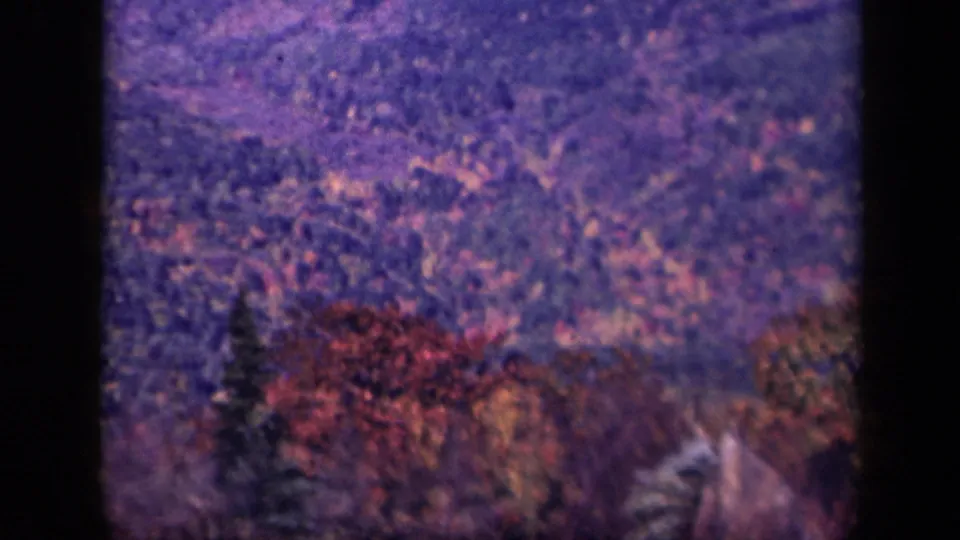 1943 Skyline Drive home-movie frame showing a narrow road cutting through wooded Blue Ridge slopes under a hazy sky.