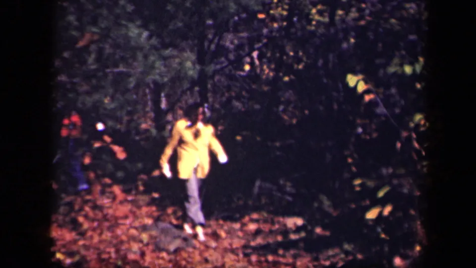 Adult in a yellow jacket walks along a leaf-covered forest path in the 1943 Skyline Drive home-movie footage.