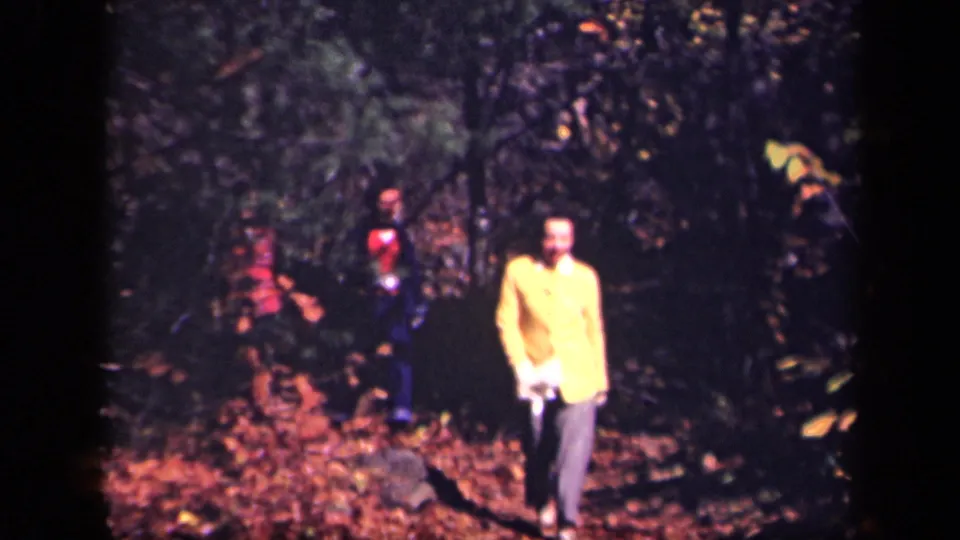 1943 Skyline Drive forest scene with an adult in a yellow jacket near the camera and additional adults partly visible behind trees.