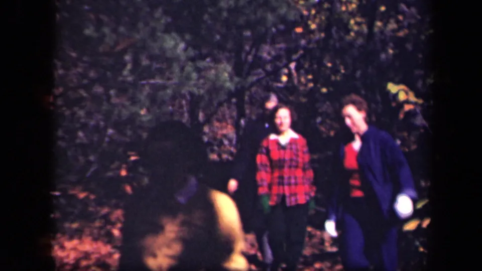 1943 8mm frame from Skyline Drive showing two adults smiling or facing the camera while walking through autumn woods.