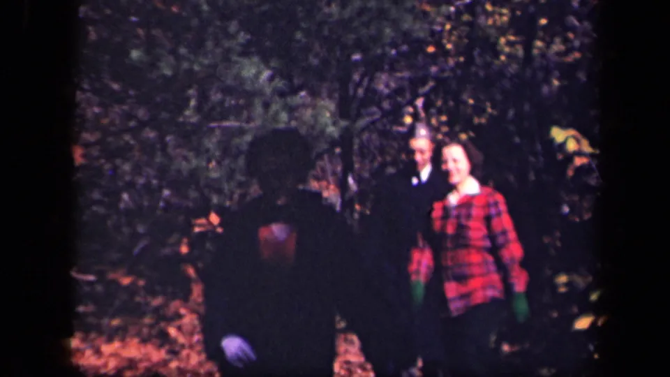 1943 Skyline Drive home-movie frame with two adults near the path and a dark foreground figure partially blocking the view.