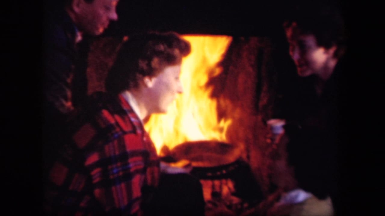 1943 Skyline Drive home-movie frame showing adults gathered close to a campfire at night, lit by orange flame.