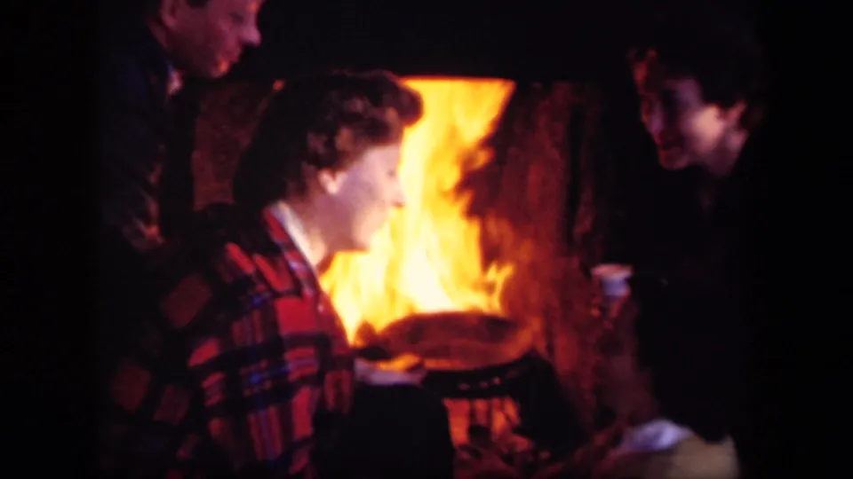 1943 Skyline Drive home-movie frame showing adults gathered close to a campfire at night, lit by orange flame.