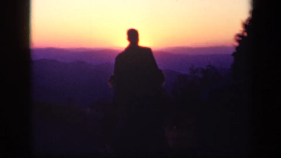 A silhouetted man stands still before a warm Skyline Drive sunset, with layered Virginia mountains in the distance.