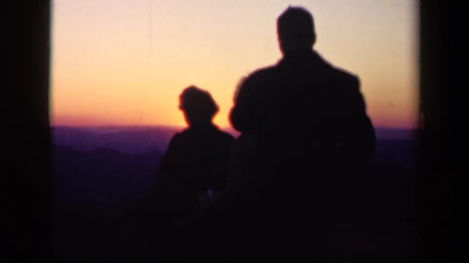 A woman and man appear as dark silhouettes against the fading Skyline Drive sunset in soft 8mm footage from 1943.