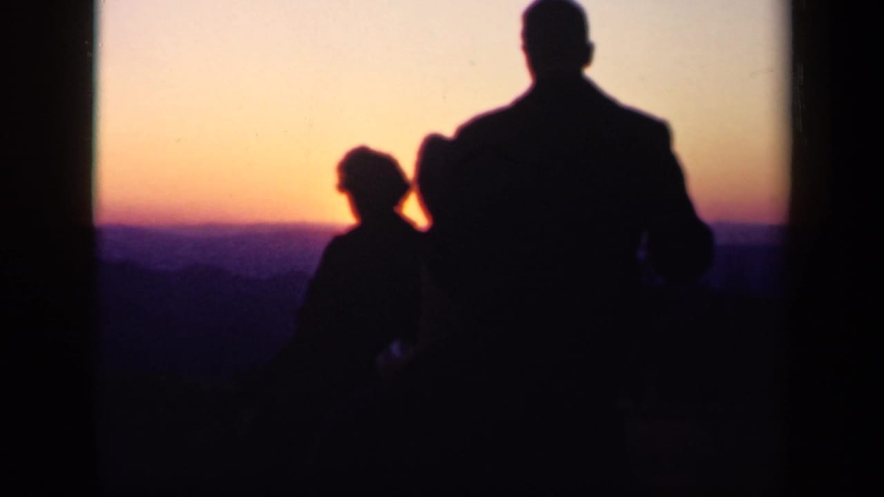 A standing adult and smaller figure appear in silhouette against a fading sunset.