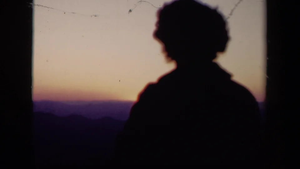 Silhouetted person in 1940s 8mm home-movie footage looking toward a warm sunset over distant ridgelines at Skyline Drive, Virginia.