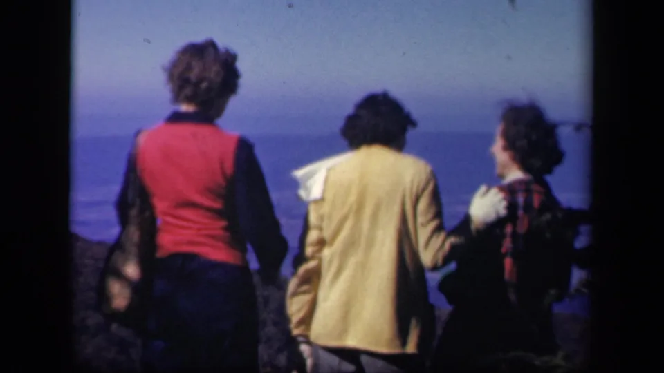 The three women remain at the Skyline Drive viewpoint, framed by dark trees and a soft blue distant landscape.