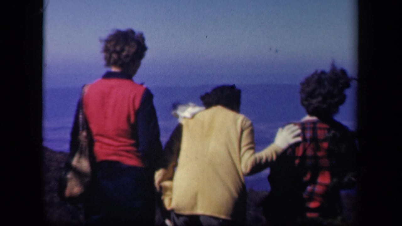 Three women stand close together with their backs to the camera at a scenic overlook.