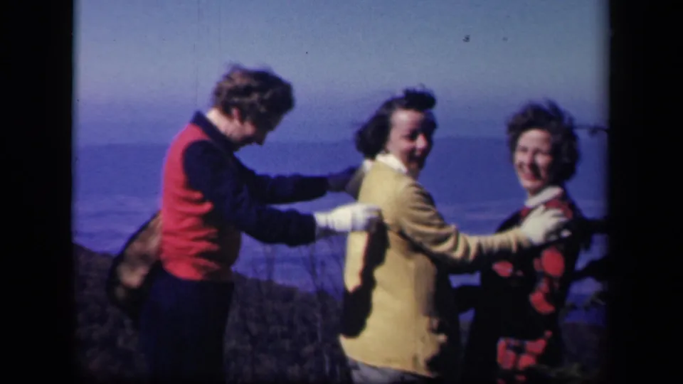 The three women laugh and turn together at Skyline Drive, with gloves and colorful outerwear visible in the 1943 home movie.