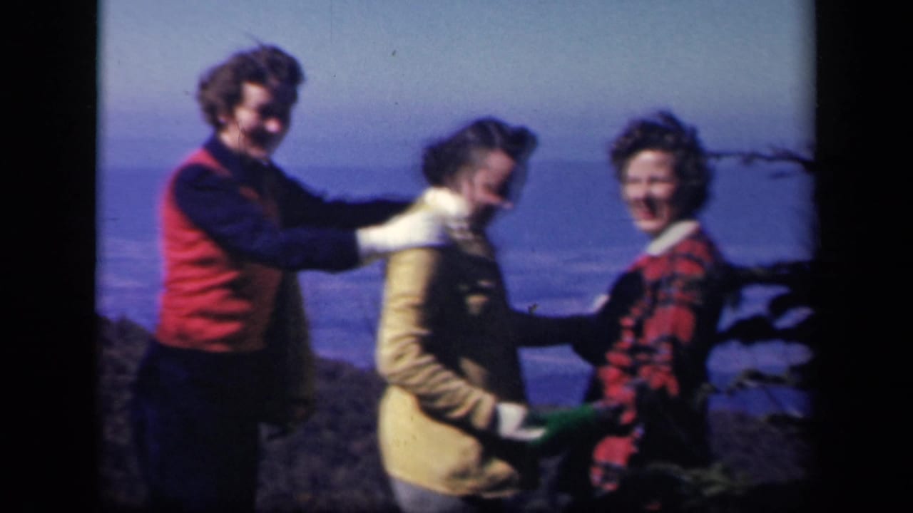 Three adults in winter clothing pose near a rocky overlook with distant scenery behind them.