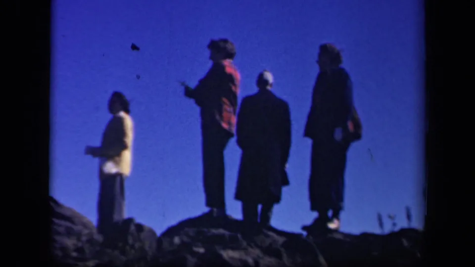 Four adults in coats stand along a rocky Skyline Drive overlook, their figures darkened by backlighting.