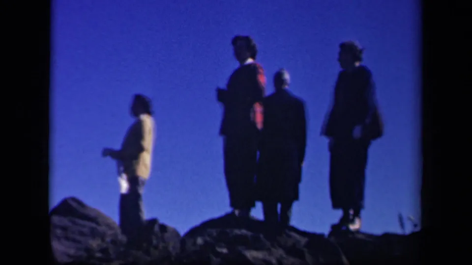 Four adults stand in silhouette on the rocky Skyline Drive overlook, including one figure in a light coat at left.