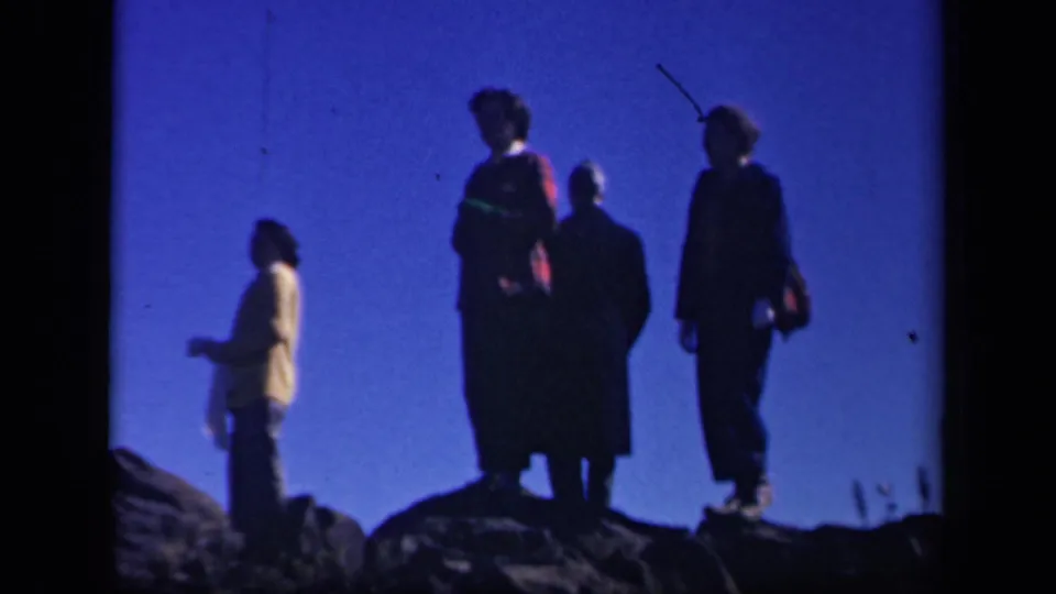 Four women on a rocky Skyline Drive overlook in 1943, silhouetted against a saturated blue sky in 8mm home-movie footage.