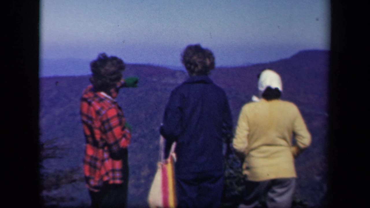 Three women stand with their backs to camera, looking over mountain ridges.