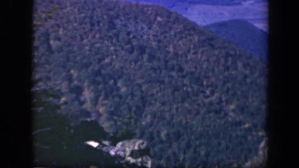 1943 Skyline Drive frame with a forested mountain ridge, rocky foreground, and distant blue ridges.