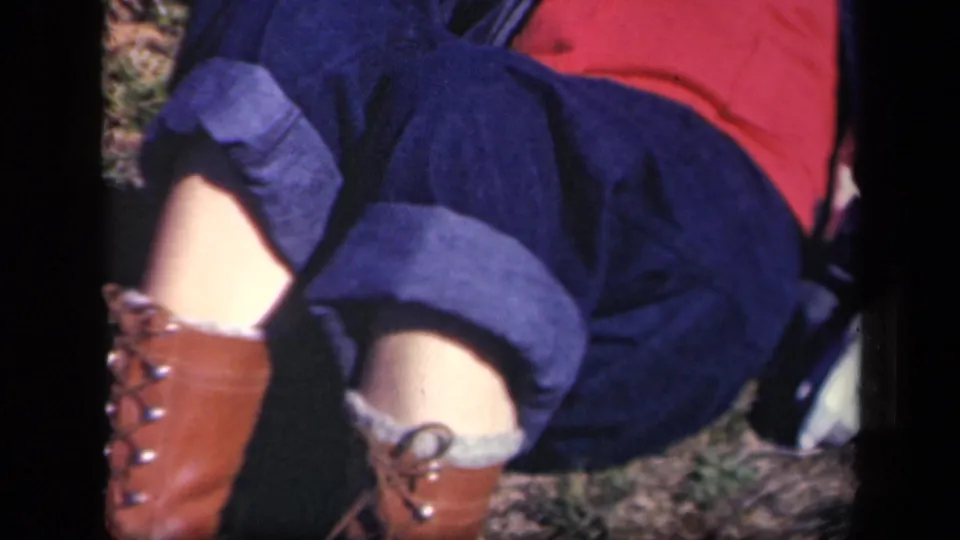 A 1943 Skyline Drive frame shows a person's lower body in blue jeans, brown boots, and red clothing against outdoor ground.
