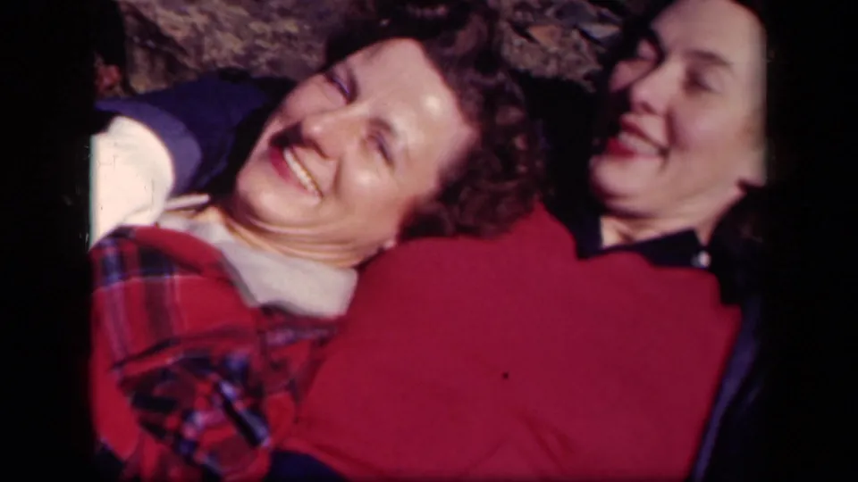 Two adult women laugh together while lying on the ground in 1943 Skyline Drive home-movie footage.