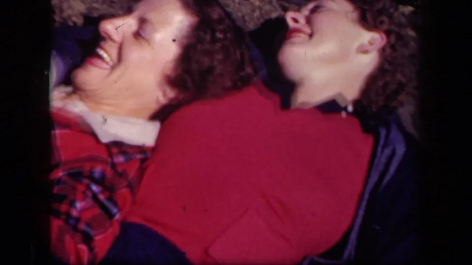 Two women laugh with heads tilted back in a 1943 Skyline Drive home-movie frame, with soft focus and strong color saturation.