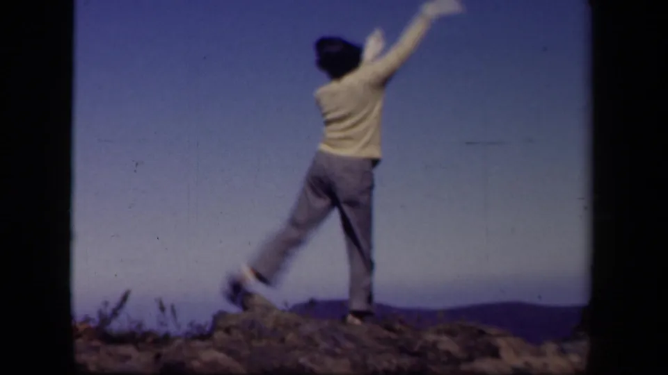 The hilltop dancer moves across rocky ground with one arm lifted, framed by sky and distant Virginia ridges.