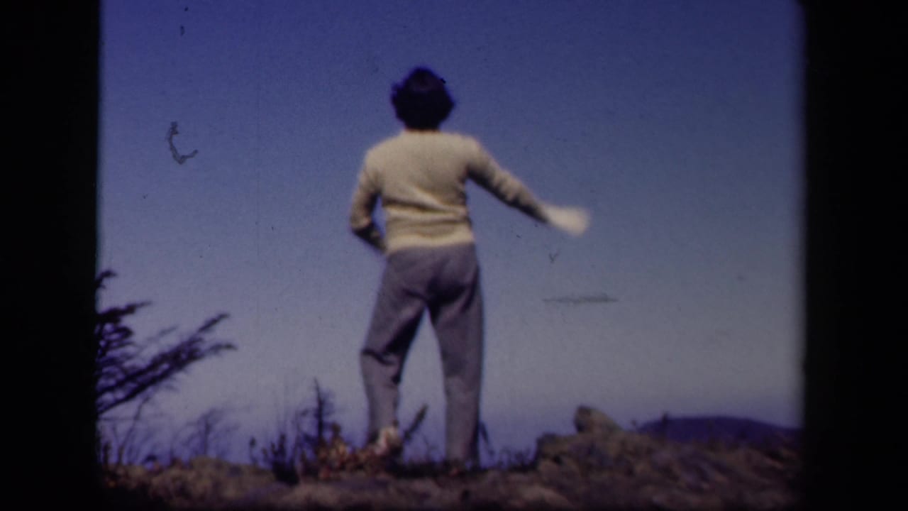 In 1943 Skyline Drive home-movie footage, a woman stands with her back to the camera on a rocky ridge beneath a deep blue sky.