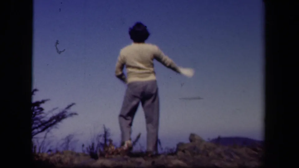 In 1943 Skyline Drive home-movie footage, a woman stands with her back to the camera on a rocky ridge beneath a deep blue sky.