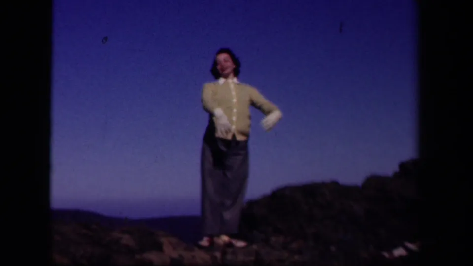 The woman turns toward the camera on the Skyline Drive ridge, with distant hills and a blue sky in the background.