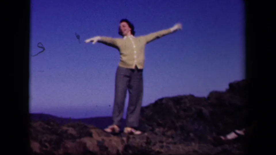 The woman spreads her arms wide on the Skyline Drive overlook, standing on rocks with hills low on the horizon.